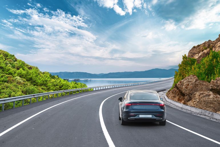 Electric car on the coast road on the shore of the lake. car driving on the road of europe. Highway view on the coast on the way to summer vacation. Germany trip on beautiful travel road landscape.; Shutterstock ID 2564215775; purchase_order: aj; job: ; client: ; other:
