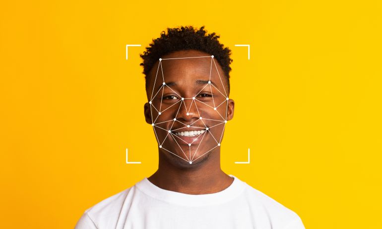 A smiling individual sits against a vibrant yellow background, with facial recognition technology overlay capturing key features. The scene highlights modern identification methods.