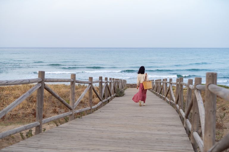 Woman Walking on Wooden Pathway with Straw Bag