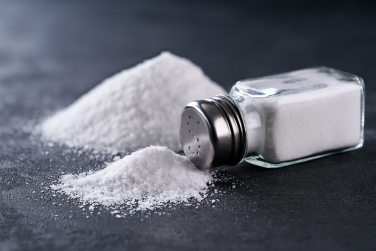 Salt shaker and pile of spilled salt crystals on a black table, selective focus.