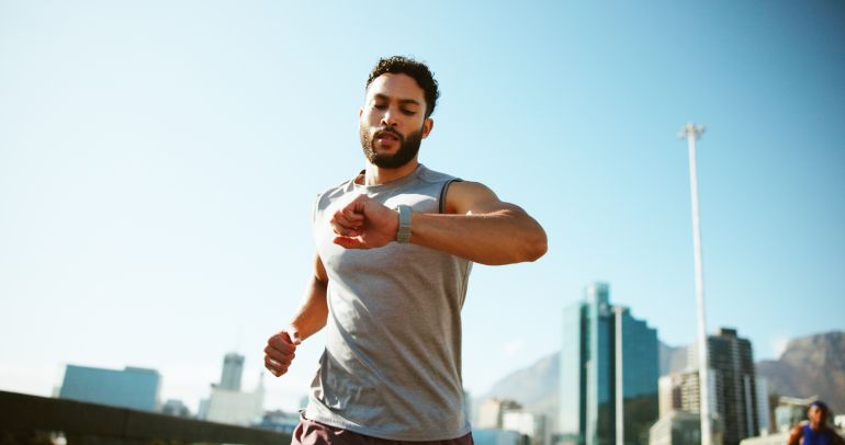 Man, fitness and running with watch in city for workout app, exercise or tracking performance. Active, male person or runner checking wristwatch for steps, calories or monitoring heart rate in town