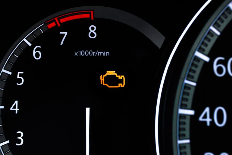Check engine light or warning light closeup, Closeup of a car dashboard with an illuminated check engine light and the tachometer displaying engine revolutions per minute.