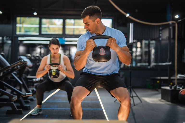 Personal coach do kettle bell squat exercise with client at gym. Athletic couple doing kettle bell goblet squat exercise during cross training in gym