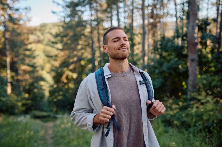 Young male hiker breathing fresh air and enjoying the peaceful nature during trekking in the forest