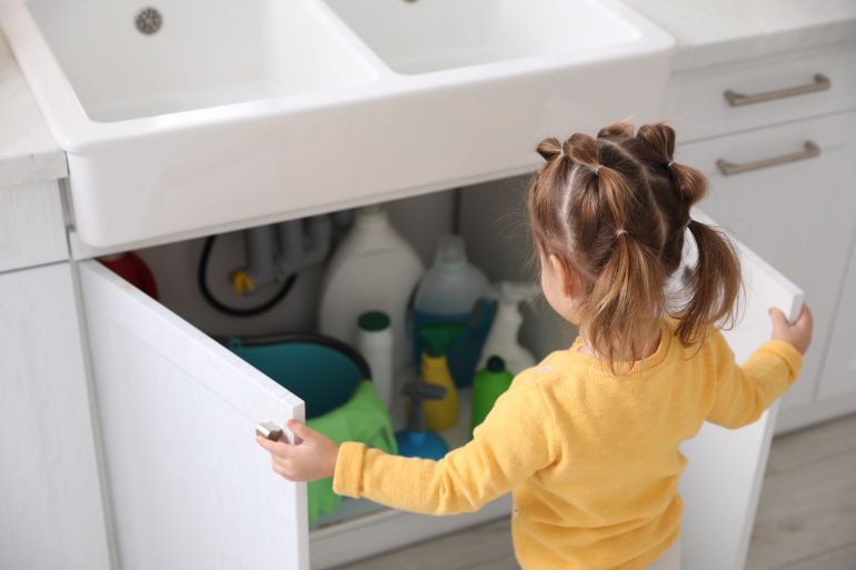 Child safety at home. Little girl opening cabinet with cleaning products in kitchen