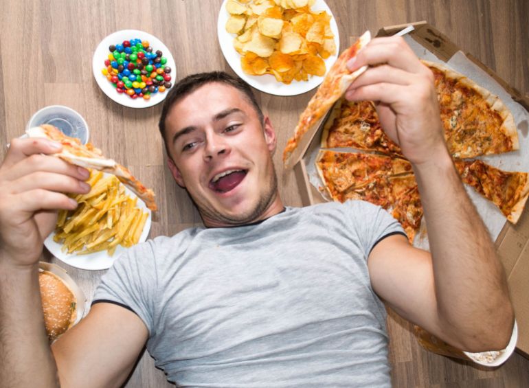 Unhealthy concept. beautiful athletic guy with unhealthy food: pizza, lemonade, chips, candy and chips.