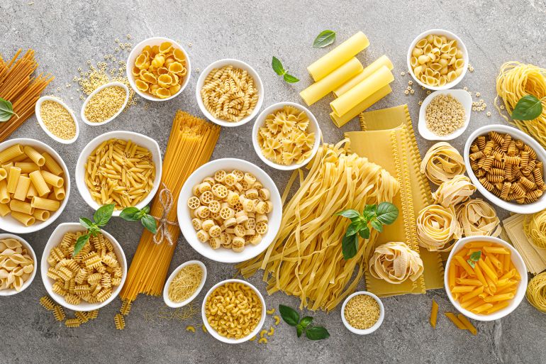 Pasta. Various kinds of uncooked pasta and noodles over stone background, top view with copy space for text. Italian food culinary concept. Collection of different raw pasta on cooking table