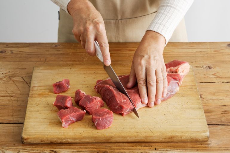56t6-1746624421 Woman slicing meat on wooden board