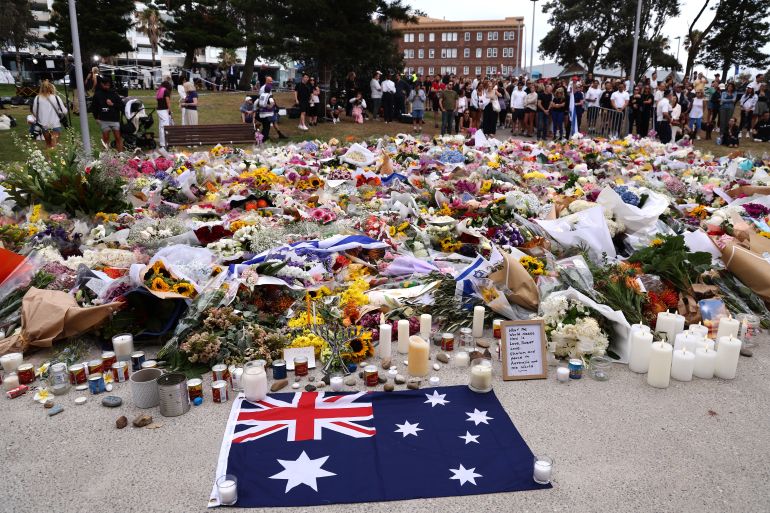 afp_6940de0f97f6-1765858831 TOPSHOT - Mourners gather around floral tributes at Bondi Pavilion to honor the victims of the Bondi Beach shooting in Sydney on December 16, 2025.