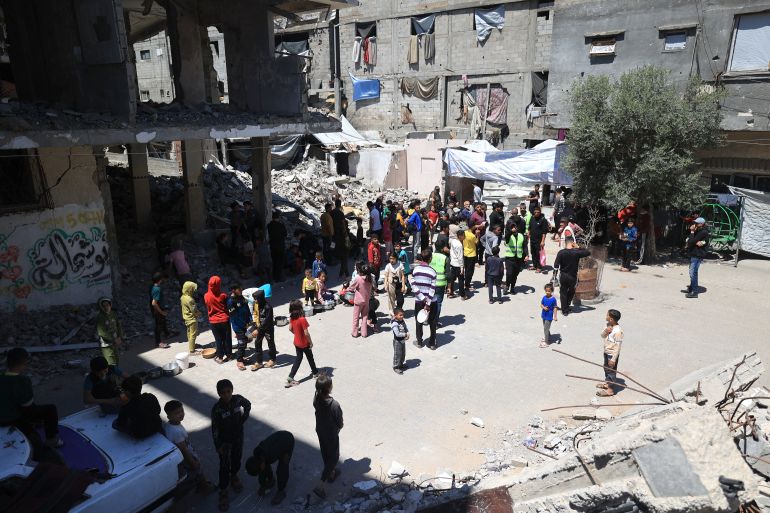Displaced Palestinians stand near the rubble of buildings destroyed by the Israeli military, as they wait to collect food from a charity kitchen in the Bureij refugee camp, in the central Gaza Strip on May 1, 2026.