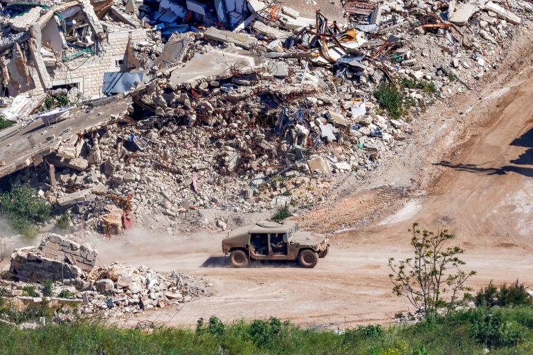 TOPSHOT - An Israeli army humvee vehicle moves past destroyed buildings in southern Lebanon as seen from across the border at a position in northern Israel on May 7, 2026.