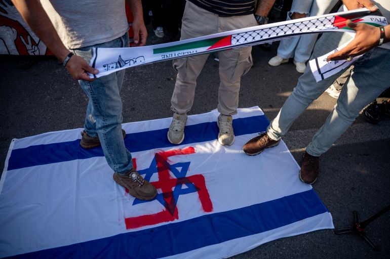 Protesters stand on an Israeli flag on which a red swastika is painted over the Star of David during a gathering against the interception of the Global Sumud Flotilla by the Israeli Navy off the coast of Cyprus outside the Ministry of Foreign Affairs in Athens on May 18, 2026.