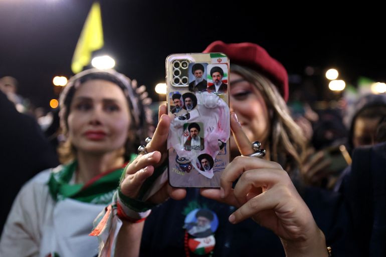 TOPSHOT - A woman with her mobile phone containing photos of Iran's current supreme leader Ayatollah Mojtaba Khamenei and his predecessor and late father Ayatollah Ali Khamenei, takes pictures of the farewell ceremony of Iran's national football team ahead of their departure for the 2026 FIFA World Cup, in Tehran on May 13, 2026.