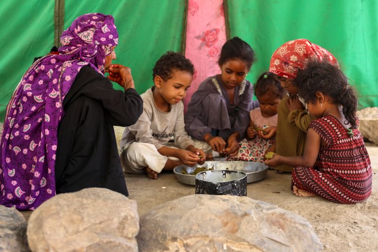 afp_6a1333b6b2aa-1779643318 Displaced Yemeni woman Saeedah Mohammed along with her grand-children, eat boiled tree leaves inside their makeshift tent in the Al-Manij displacement camp, near the city of Taez in Yemen's southwest, on May 21, 2026.
