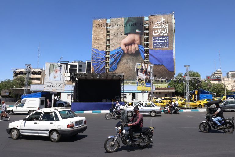 afp_6a1442e3d591-1779712739 Vehicles drive past a billboard on the facade of a building depicting the Strait of Hormuz with a caption in Persian reading "Forever in Iran’s Hand", at Vanak Square in Tehran on May 25, 2026.