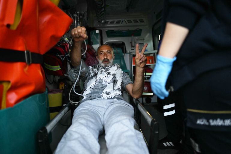 A member of the Global Sumud Flotilla headed for Gaza and arrested and deported by Israel gestures the V-sign and a raised fist as he is loaded into an ambujlance following the group's arrival at Istanbul Airport on May 21, 2026.