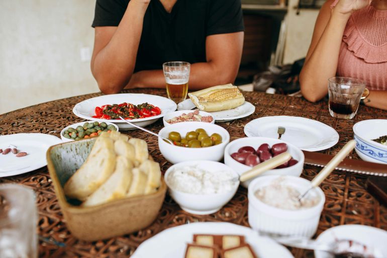 alakl-alshy-1779347681 A variety of Mediterranean dishes on a table with bread, olives, and drinks for a casual gathering.