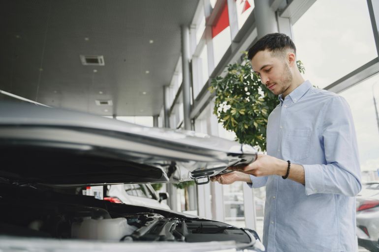 alsyant-1778923645 Young man checking car engine in modern dealership showroom.