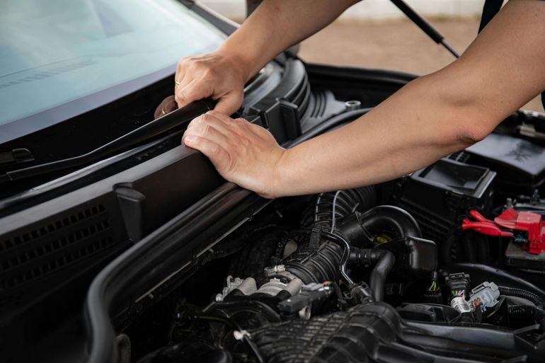alsyant3-1778924353 Close-up of hands repairing a car engine outdoors, focusing on automotive maintenance.