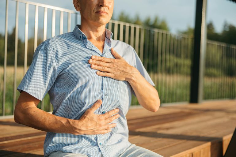 A man practicing relaxation with hands on chest and abdomen outdoors