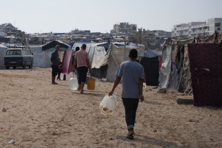 Displaced Palestinian carry jerrycans filled with water through a tent camp in Khan Younis, in the southern Gaza Strip, Thursday, April 30, 2026. (AP Photo/Abdel Kareem Hana)