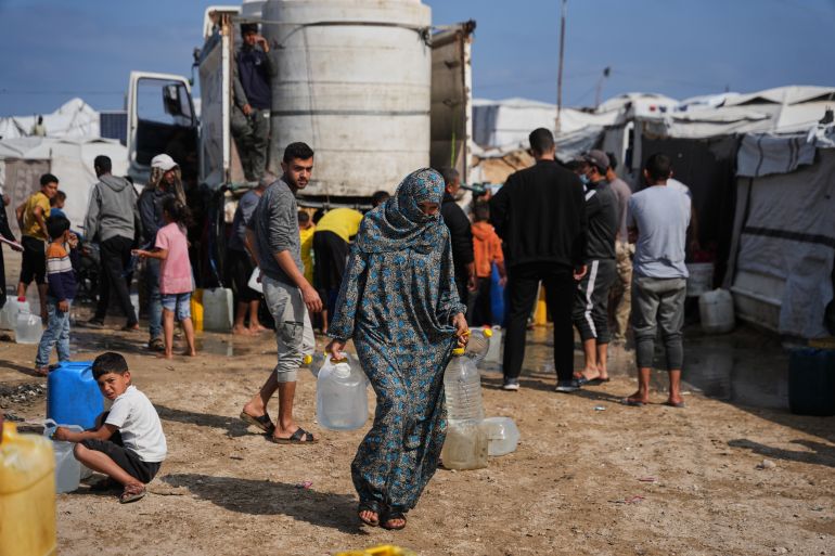 ap_69f707da12560-1777797082 Samah Abu Daqqa, 33, carries jerrycans filled with water through a tent camp in Khan Younis, in the southern Gaza Strip, Thursday, April 30, 2026. (AP Photo/Abdel Kareem Hana)