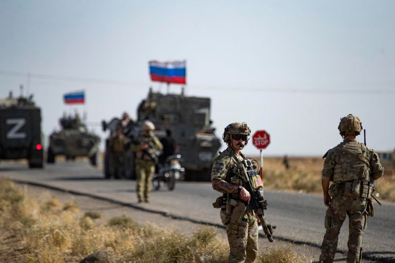 Soldiers of a Russian military convoy and their US counterparts exchange greetings as their patrol routes intersect in an oil field near Syria's al-Qahtaniyah town in the northeastern Hasakah province, close to the border with Turkey, on October 8, 2022. (Photo by Delil SOULEIMAN / AFP)
