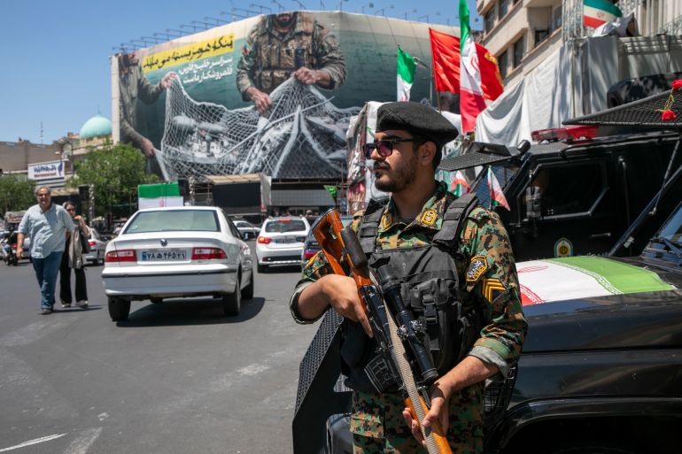 TEHRAN, IRAN - MAY 9: An Iranian police office stands on patrol near a poster depicting Iranian soldiers holding a net in the shape of the Strait of Hormuz, with US military aircraft ensnared in a fishing net, on May 9, 2026 in Tehran, Iran. There is little sign of progress in negotiations between Iran and the United States, despite both sides' insistence that their monthlong ceasefire is holding. (Photo by Majid Saeedi/Getty Images)
