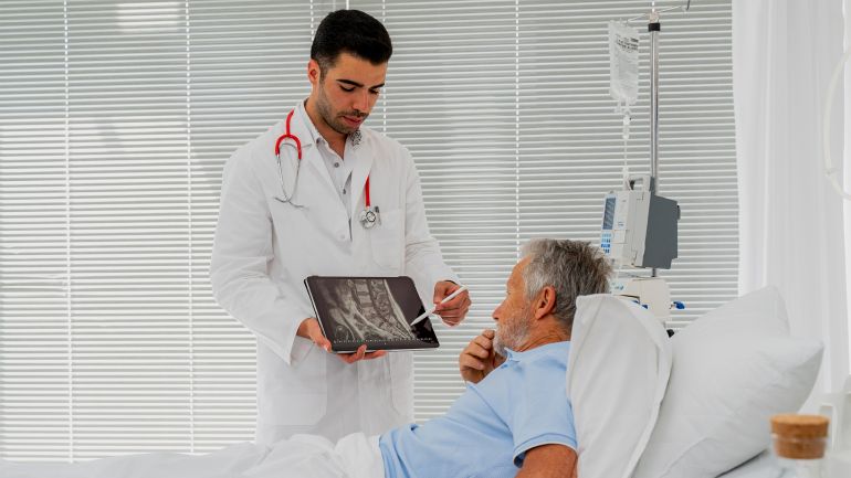 gettyimages-1400863470 غلاف فيديو بعنوان: هل هشاشة العظام حكر على النساء؟ This is why you're feeling pain - stock photo Hospital Ward: Friendly Doctor Talks to Senior male Patient Resting in Bed, Young Doctor using a Digital Tablet during a Consultation with a Senior Man GettyImages-1400863470