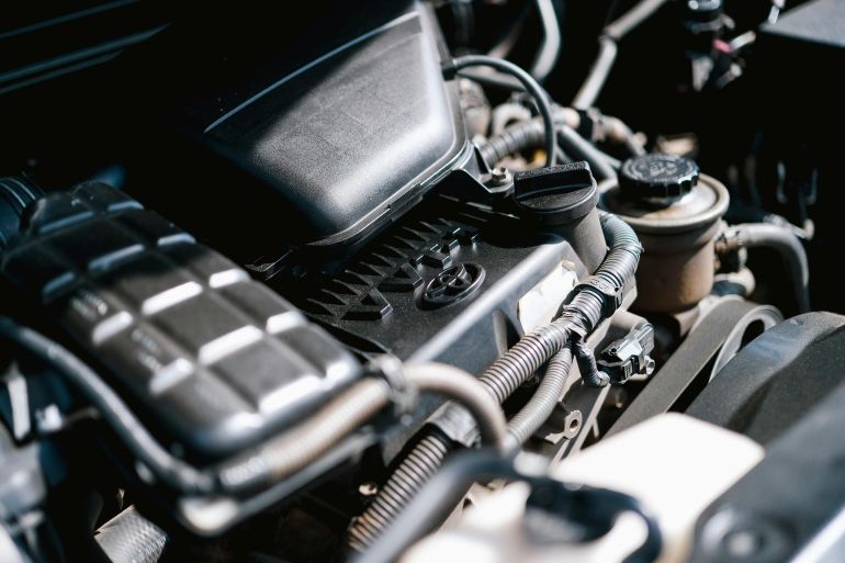 ghyar-1779111406 Detailed view of car engine parts, showcasing cables and components with bright lighting.