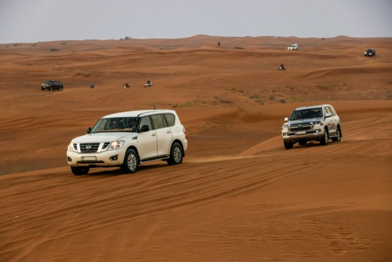 jnwd-alshracabe-1779387302 White 4x4 vehicles driving across sandy desert dunes during a thrilling safari adventure.