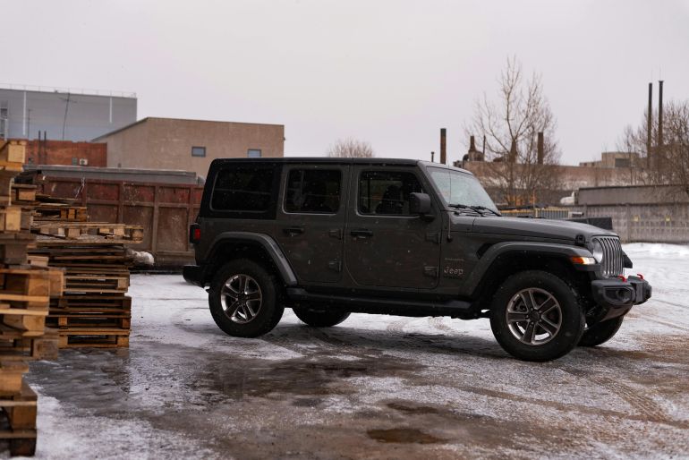 jyb-1779385681 A rugged SUV parked outdoors in a snowy industrial area, surrounded by pallets.