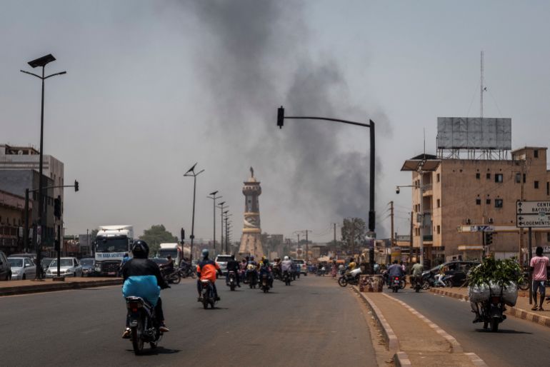 A column of black smoke rises above buildings as traffic passes the Africa Tower monument in Bamako on April 26, 2026. April 25, 2026's shock attacks, synchronised by Tuareg rebels of the Azawad Liberation Front (FLA) coalition and the jihadist Group for the Support of Islam and Muslims (JNIM), targeted several areas in the vast arid country. Fighting resumed on April 26 in several areas, including Kita near Bamako, Kidal, Gao and Severe. Tuareg rebels meanwhile announced an agreement allowing Russian forces backing Mali's army to withdraw from the northern city of Kidal, which they claimed was "totally" under their control. (Photo by AFP)