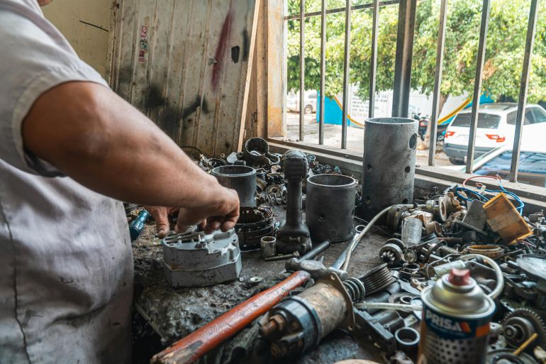 qtcabf-ghyaar-1779111507 Mechanic organizing auto parts in a busy workshop, surrounded by tools and equipment.