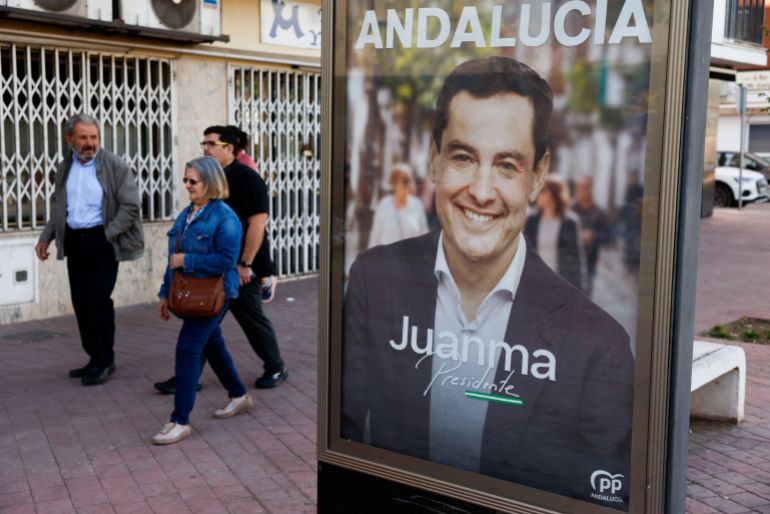 reuters_6a0aaf9b-1779085211 People walk past an electoral poster of Andalusian regional president and People's Party (PP) candidate, Juanma Moreno Bonilla, during the Andalusian regional elections in Ronda, Spain May 17, 2026. REUTERS/Jon Nazca