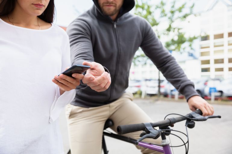 Male Thief Riding On Bicycle Snatching The Mobile Phone From Woman's Hand Walking On Street