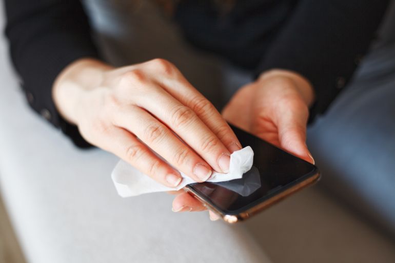 Hands wiping down mobile phone’s surfaces due to corona virus crisis.