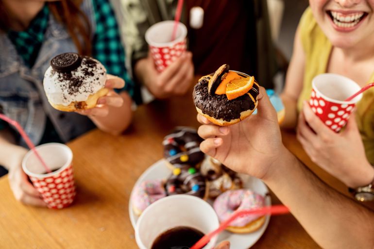 Close-up of friends eating various glazed donuts while gathering in a cafe.