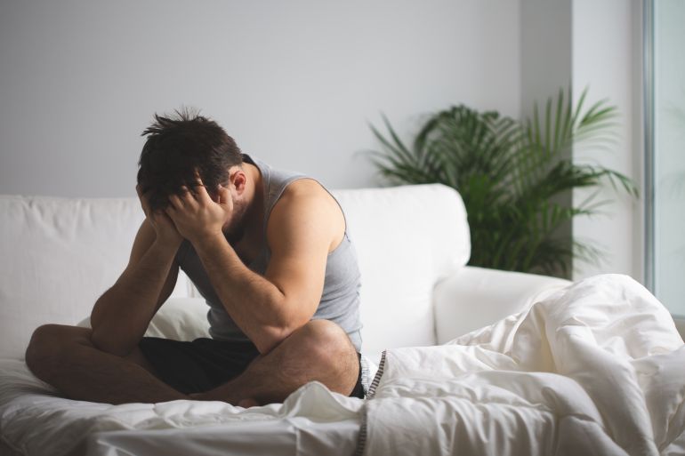 Young man suffering from insomnia sitting on his bed