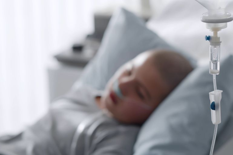 Focus on intravenous drip with sick kid lying in hospital bed on background. Teen boy patient with cancer resting in bed having medication in dropper; Shutterstock ID 1921349711; purchase_order: aj; job: ; client: ; other: