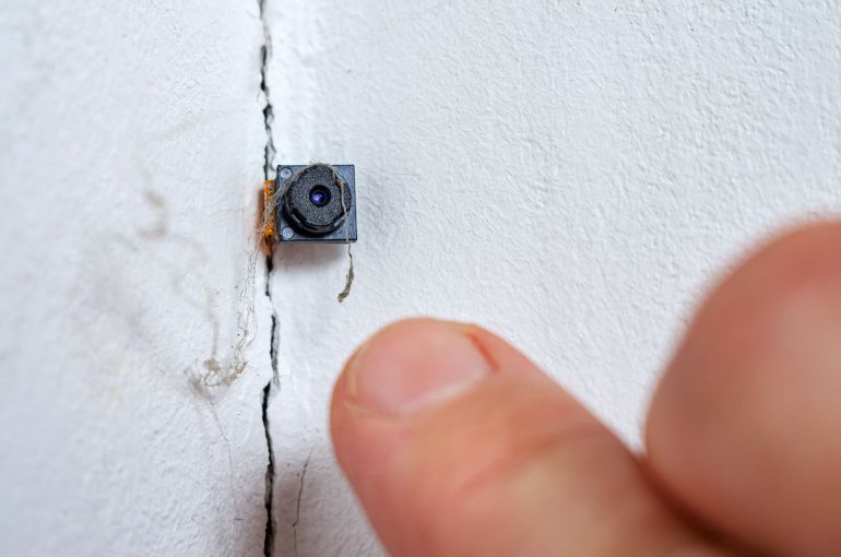 Spy hidden camera in the crack of the wall. Man discovers micro camera in office. Spy scandal, collecting compromising evidence, wiretapping, symbolic image.