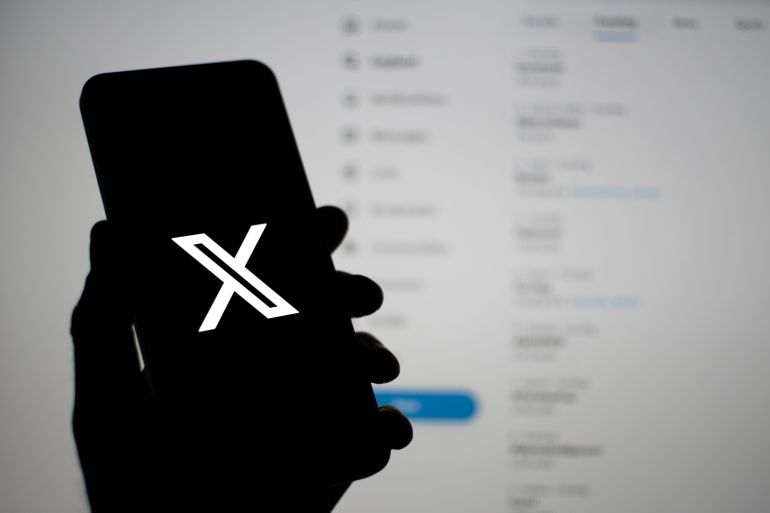 Guildford, UK - November 2, 2023: Hand holding a smartphone with X app logo in front of Trending screen background. Formerly known as Twitter, X is a social media platform currently owned by Elon Musk