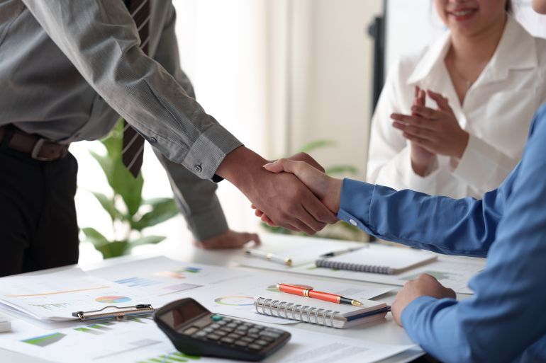 Businessmen shake hands to end the meeting. Successful negotiations and handshakes Group of business people congratulating each other inside the office.