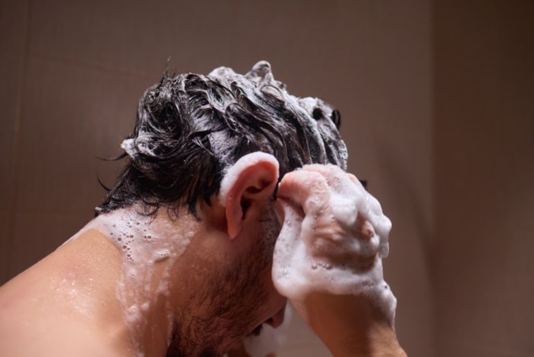 shutterstock_2468479769-1780216802 Close-up of a man washing his hair with shampoo, creating a rich lather, representing personal hygiene.
