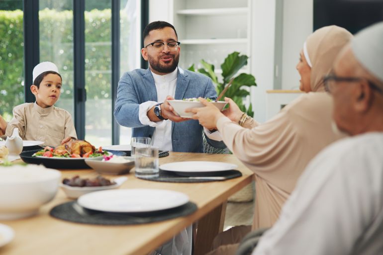 Muslim, family and dinner in home for eid, islamic celebration and serving food on dining table. Ramadan, culture and religious gathering with conversation, eating and people hosting with lunch; Shutterstock ID 2471690139; purchase_order: aj; job: d; client: d; other: d