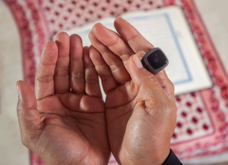 Close up of Asian Muslim woman's hand using modern digital prayer beads while praying after reading the Quran