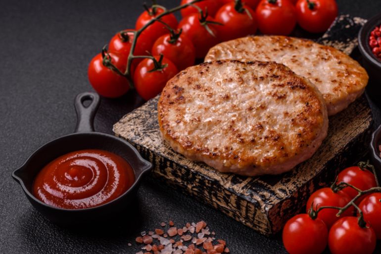 shutterstock_2560773103-1779266400 Grilled chicken burger cutlet with salt, spices and herbs on a dark concrete background