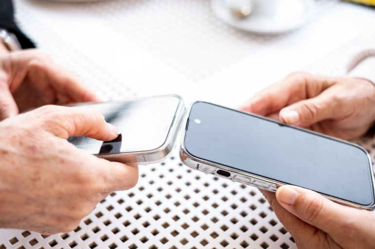 Close up view of two modern women's hands using apps and wireless technology to share files or photos between their smartphones