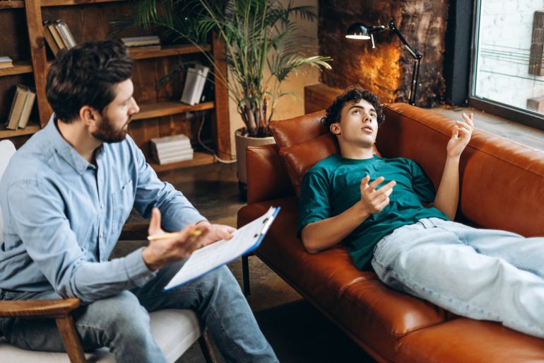 Portrait of professional male psychotherapist working with teenager boy in office, making notes. Psychotherapy services, mental health professional concept