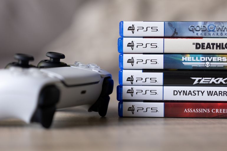 shutterstock_2634814873-1779275162 Brecht, Belgium - 18 april 2025: A stack of sony playstation 5 videogame cases or boxes lying on a wooden table next to a wireless PS5 controller. Ready to play a console game.
